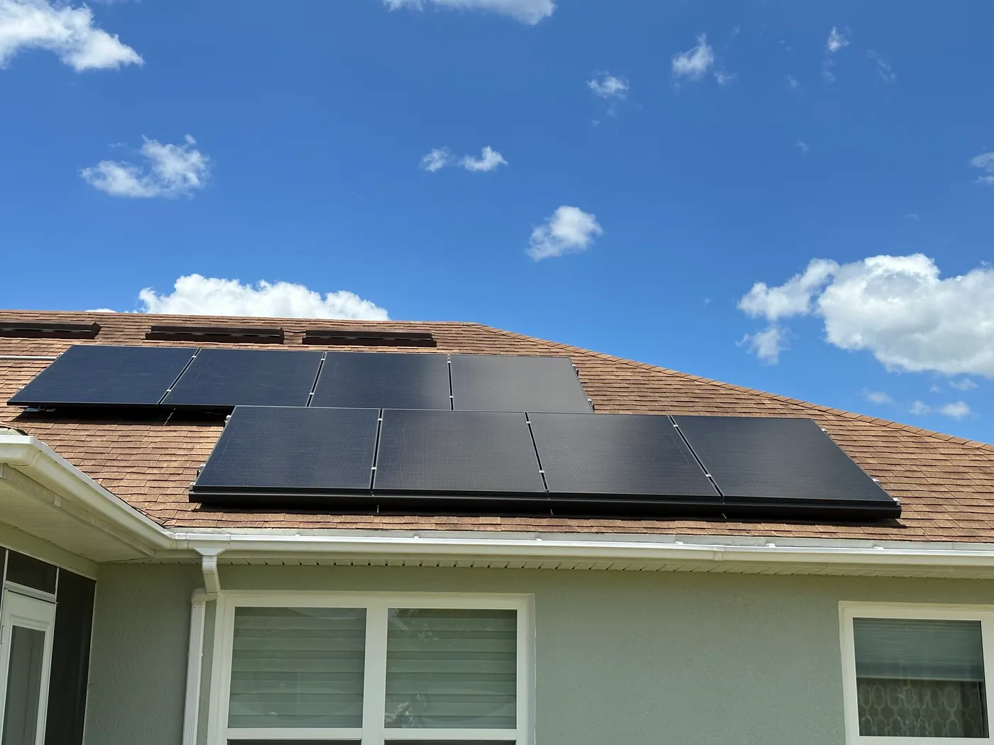 Close view of black solar panels installed on a shingle roof beneath a blue Florida sky